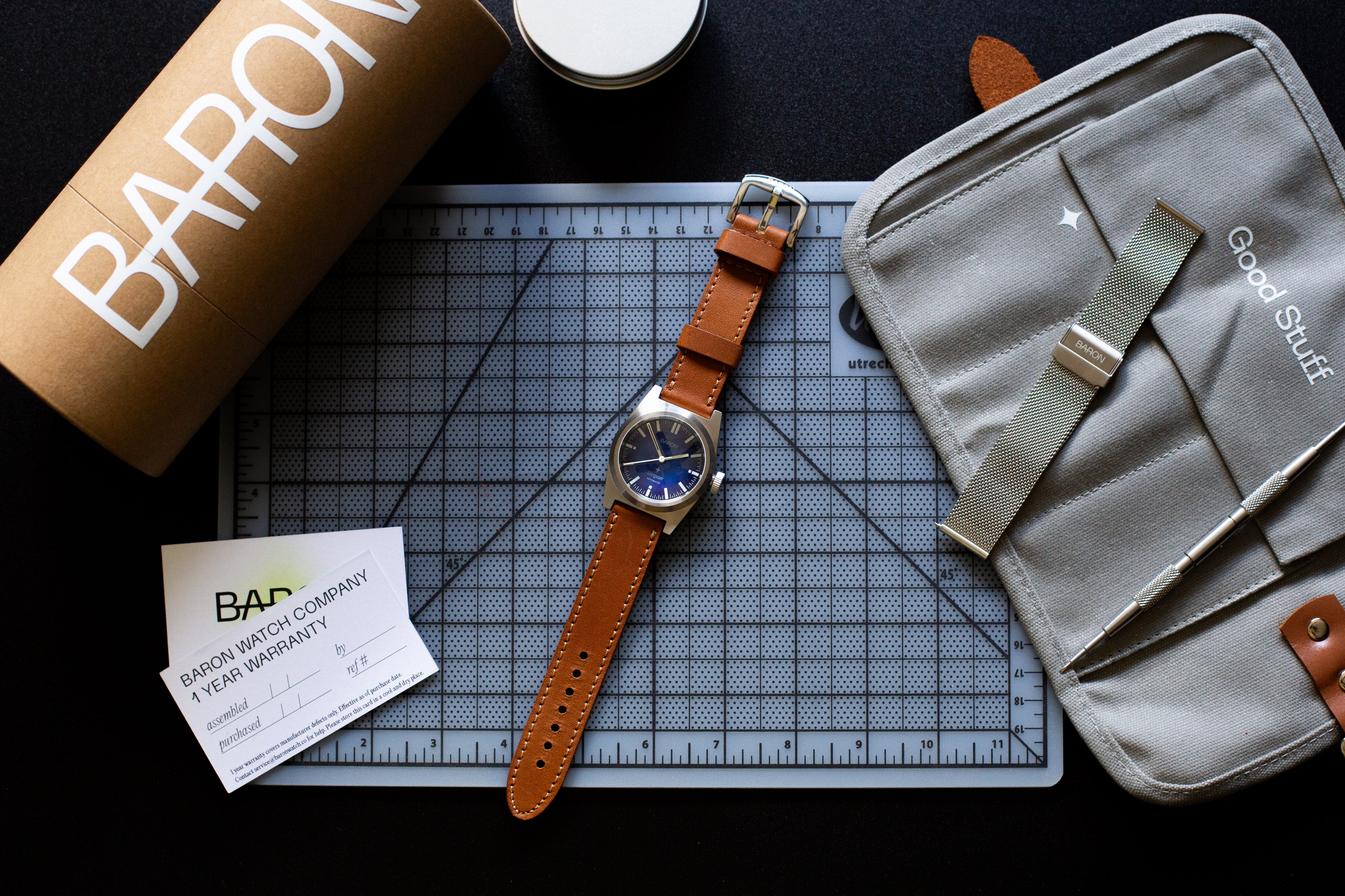Watch with brown strap on a cutting mat next to a 'Baron' branded box and a gray pouch.